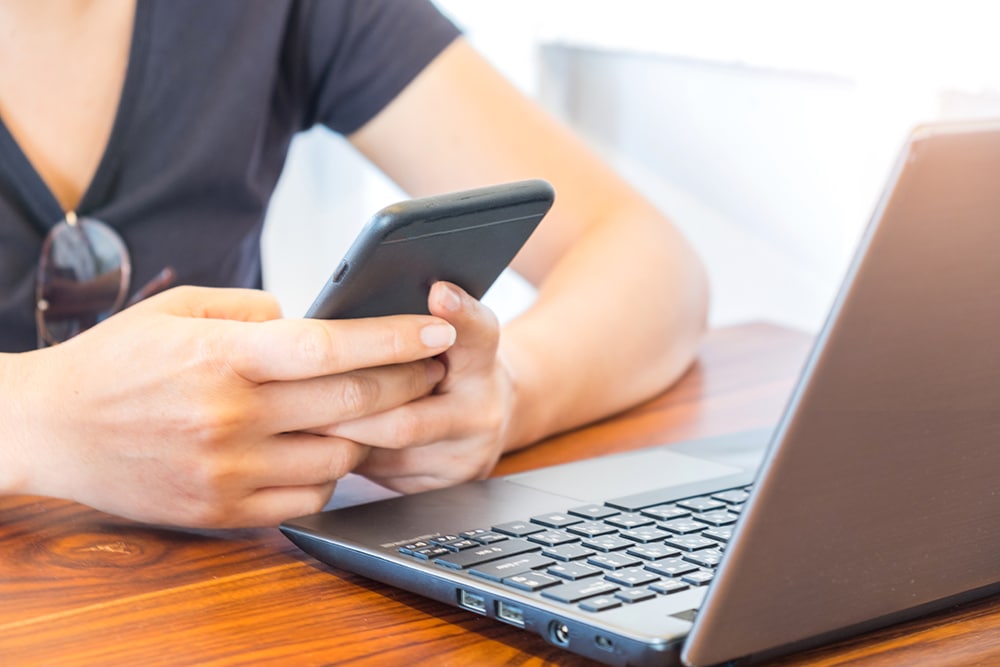 woman playing a smart phone with laptop placed in PQ9GX9W 4